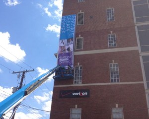 A crane lifts a banner onto the side of a building.