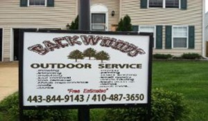 A sign for backwoods outdoor service in front of a house.
