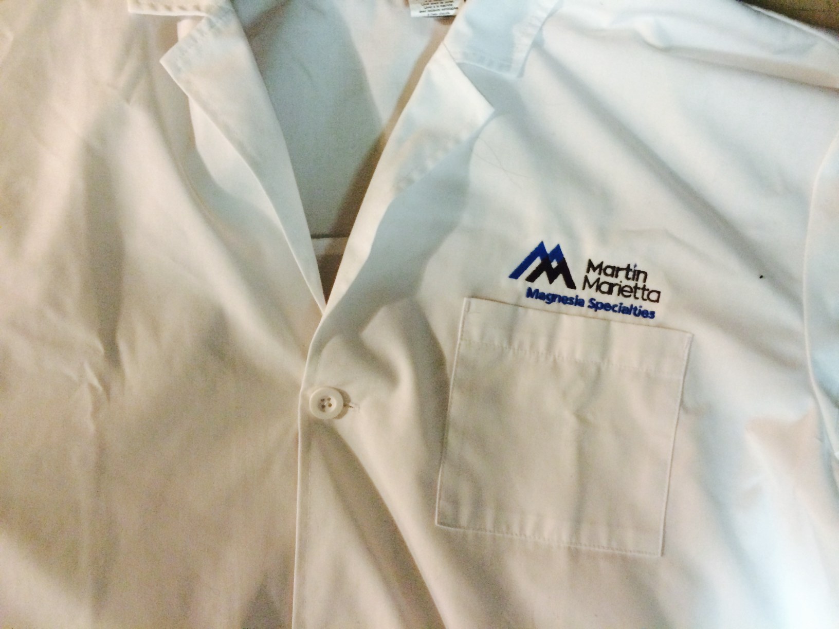 A martin marietta magnesia specialties lab coat with a logo on the pocket, displayed on a flat surface.
