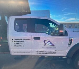 White c&a construction pickup truck with company services labeled and contact information on the door, parked outdoors.