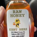 A hand holds a bottle of raw honey labeled 
