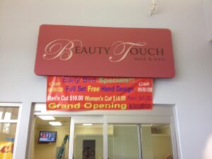 Sign for 'beauty touch hair & nail' salon advertising early bird specials and grand opening dates, inside a brightly lit venue.