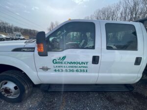 A white greenmount lawn and landscaping ford f-350 truck parked outdoors on a gravel lot.