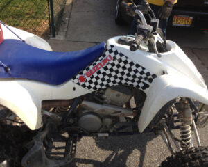 White atv with blue seat and checkered flag design parked on asphalt, license plate partially visible.