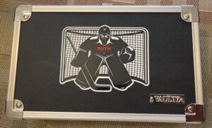 A silver briefcase with a black design featuring a hockey goalie and the name 
