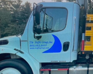 Side view of a white truck cab displaying the knife group inc. logo and contact details, with a blurred background.