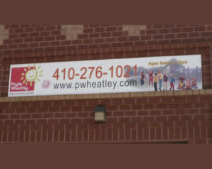 A banner on a brick wall advertising the phyllis wheatley educational center with a contact number and website, featuring cartoon images of children.