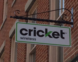A cricket wireless store sign hanging from a metal bracket on a brick building.